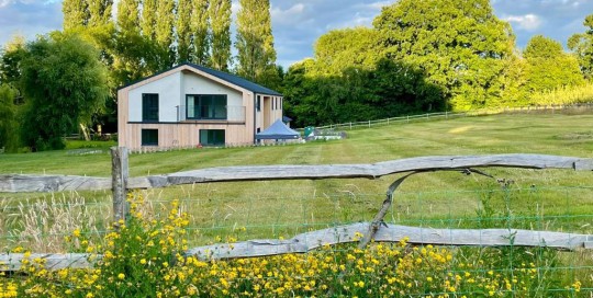 View of converted barn from across the fields. The enormous volume of the original barn was cut away in key areas to provide visual interest and private balcony areas. Timber cladding will mellow to silver grey.